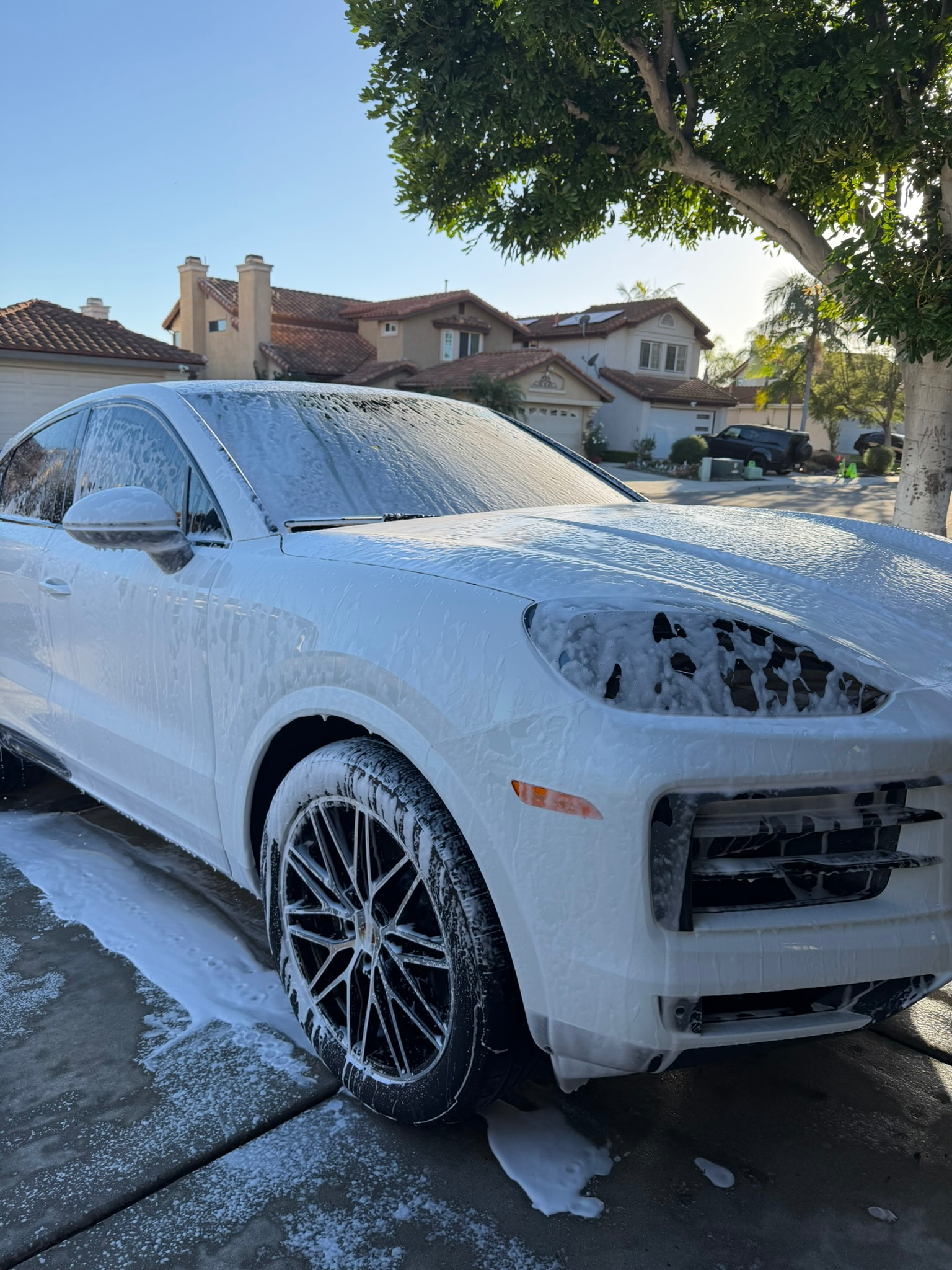 Professional mobile detailing showing white Porsche with foam pre-wash in luxury driveway